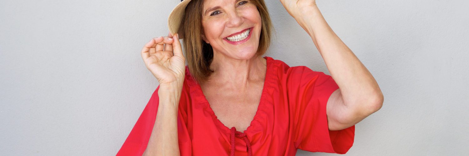 Portrait of older woman smiling with hat against gray wall