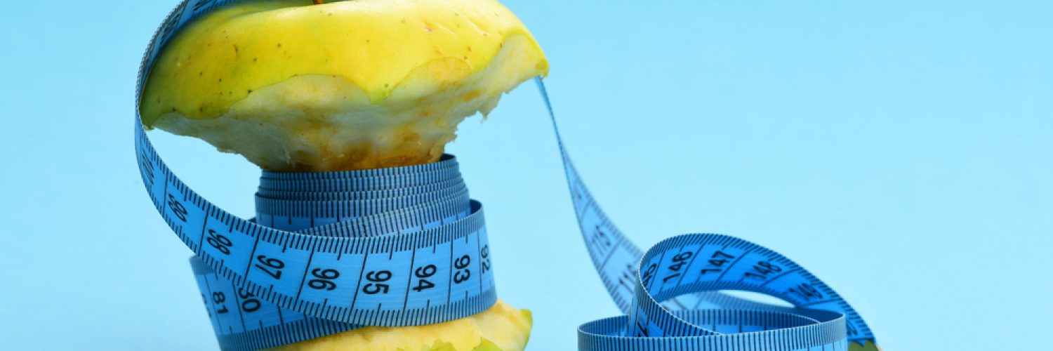 Green apple wrapped tightly with soft measuring tape on light blue background with free end rolled on the side. Diet and fitness concept