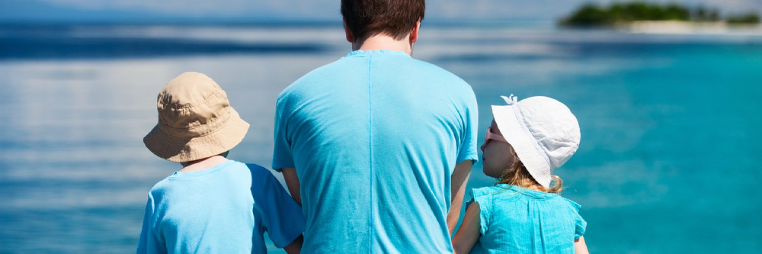 Back view of father and kids sitting on wooden dock looking to ocean