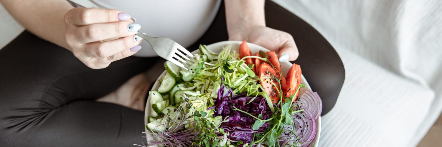 Close-up of a plate with a bright salad of fresh vegetables in the hands of a pregnant woman.