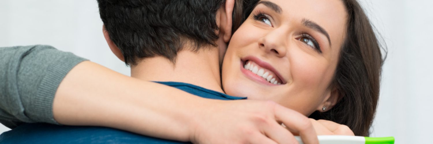 Closeup of happy young woman embracing man after positive pregnancy test