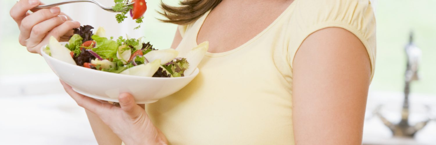 Pregnant woman in kitchen eating a salad smiling